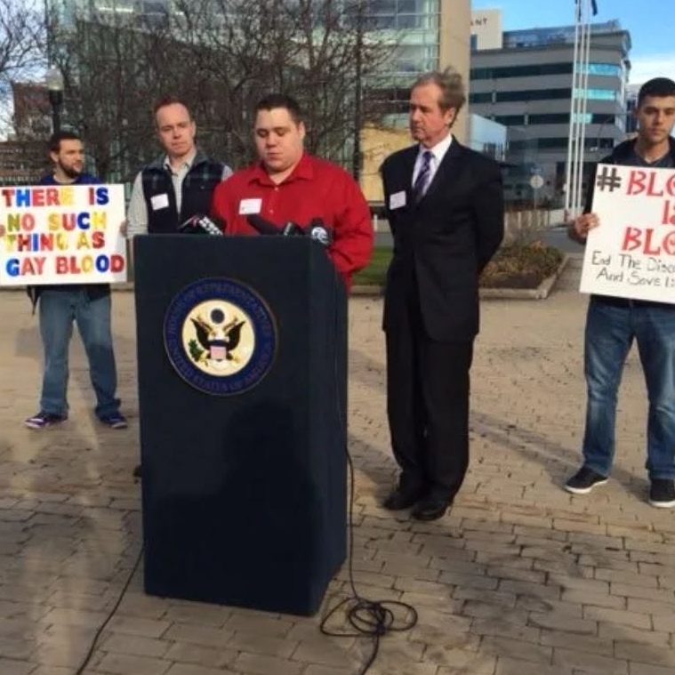 Press conference with speakers holding signs advocating for a cause.